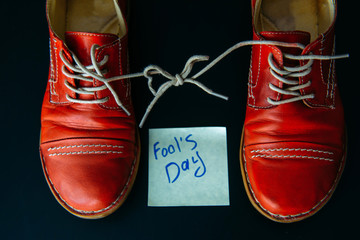 Shoes with laces tied together on black background. Shoes covered in sticky notes. April fool's day...