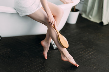 Cosmetology, Body care, Spa cosmetic products, beauty and health concept. Woman making massage legs with wooden soft massage brush for body and legs, close up, focus on legs.