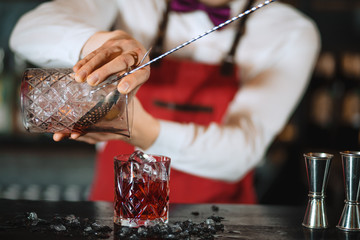 The bartender man pours ruby cocktail into crystal glass, close up, Barman is out of focus. Bar, Restaurant Beverage and Service concept.