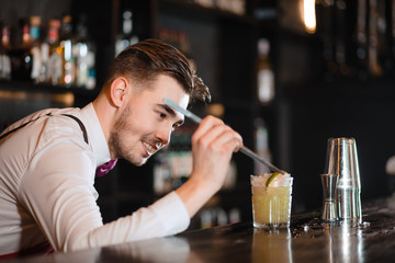 Bartender finishes decoration of his cocktail with ice cubes and lime slice