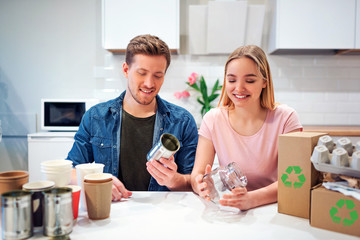 Protect the environment. Young couple recycling metal tin can and glass while sitting at the table with other waste at home