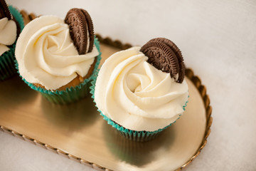 cupcakes with white cheese cream decorated with cookies on a brass tray