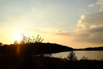 Golden sunset or sunrise with tree silhouettes over a forest lake