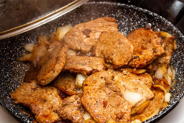 Cooking fryed meat on the pan with onion close up