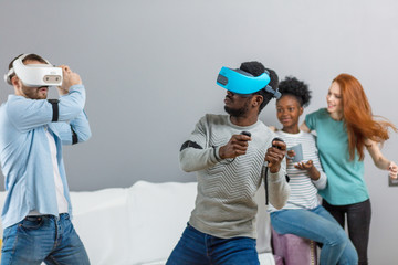 Group of multiracial male amd female students playing virtual game using vr goggles, having fun together ay home - Virtual omg reality and portable digital technologies