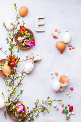 Fototapeta na wymiar Easter background with various eggs, bunny ears napkin, spring blossom branch, candies and Easter letter E on the textured surface, top view, copy space