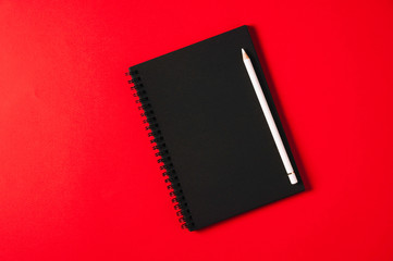 A black notebook and a white pencil on a bright red background