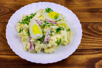 Salad with chinese cabbage, onion, sausage, eggs and mayonnaise on wooden table