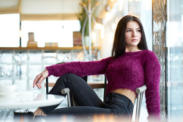 Young brunette girl sitting on chair in cafe and looking at window