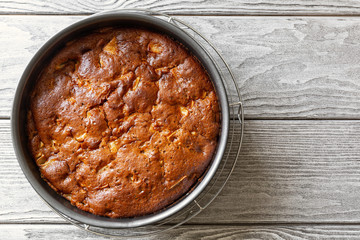 Freshly baked delicious smelling apple pie charlotte cools down in culinary form on a wooden table. Vegan apple pie without eggs, without butter, top view, flat lay