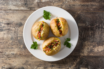 Stuffed potatoes with bacon and cheese on plate on wooden table. Top view
