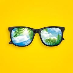 Creative layout made of black sunglasses with reflected sky cloud and tropical palm leaves, on...