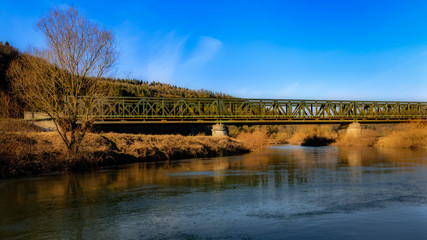 railroad bridge over a river with blue sky in the background in autumn