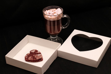 hot drink in a glass cup with pink marshmallows and white box with a transparent cover in the form of heart with cookies