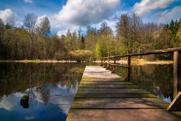 a pond with blue sky and clouds and a jetty leading into it
