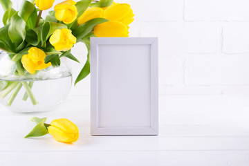 Mockup of picture frame decorated yellow tulip flowers in vase on white background with clean space for text and design