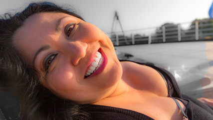 Portrait of a Mexican Latina woman with a beautiful wide smile, looking at the camera, long black hair, light makeup and a low-cut dress, enjoying the rays of the sun on a sunny day on a cruise ship
