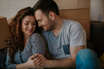 Portrait of emotional young couple hugging each other tightly. Boyfriend and girlfriend embracing sitting on the floor in their new apartment.