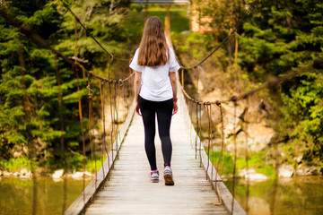 Tourist woman walk by long wooden suspension bridge above river.