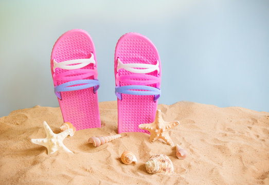 Pink flip fops, starfishes and seashells on sand beach on blue backdrop.