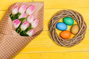 Colorful eggs and bouquet fresh tulip flowers on yellow background top view. Spring holiday. Tradition celebrate easter. Happy easter season. Easter is coming. Collecting easter eggs. Spring vibes