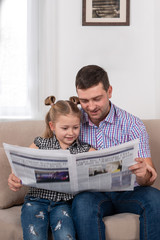 Studio shot of a daughter and dad sitting on the sofa at home and reading the newspaper together
