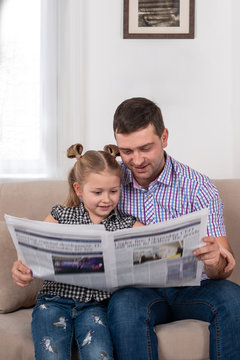 Studio Shot Of A Daughter And Dad Sitting On The Sofa At Home And Reading The Newspaper Together