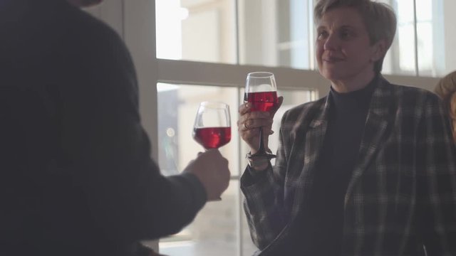 Back of man with glass of red wine and portrait of happy senior woman with grey short hair with glass of wine. Couple talk and enjoy time together. Family relationships. S-log, ungraded