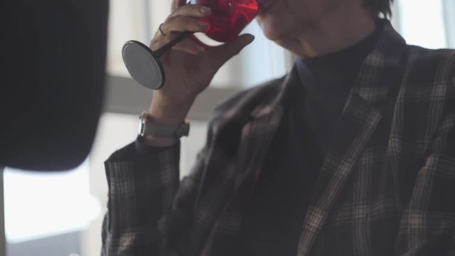 Unrecognized adult couple drinking wine from glasses sitting by the wide window. Family relationships. S-log, ungraded