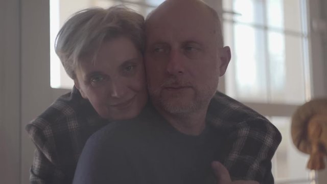 Portrait of a mature couple embracing while sitting on the floor at home. A bald man with a gray beard and a loving adult woman. S-log, ungraded