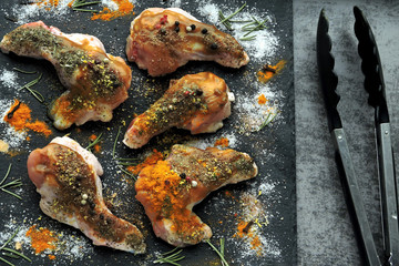 Raw chicken wings marinated in spices on a black stone board.