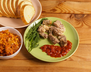 Pieces of roast meat, tomato sauce, dill bread and sauerkraut on a plate on the table.
