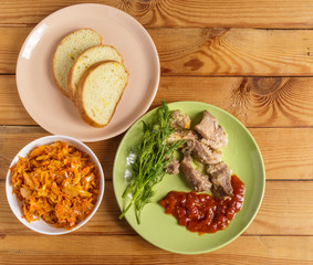 Pieces of roast meat, tomato sauce, dill bread and sauerkraut on a plate on the table.