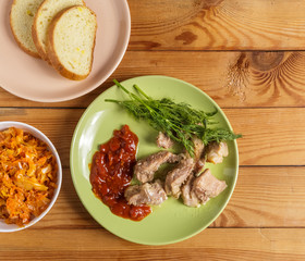Pieces of roast meat, tomato sauce, dill bread and sauerkraut on a plate on the table.