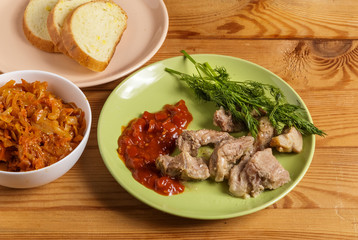 Pieces of roast meat, tomato sauce, dill bread and sauerkraut on a plate on the table.