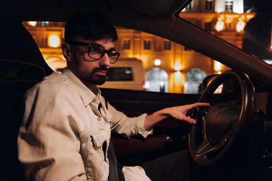 Guy with glasses driving a car at night