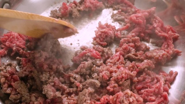 Close slow motion video of cooking hamburger in a pan with a wood spoon illuminated with natural lighting.