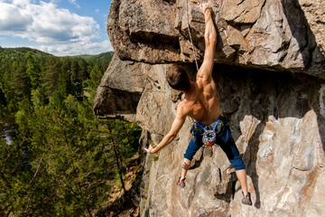 Climber Extreme climbs a rock on a rope with the top insurance, overlooking the forest