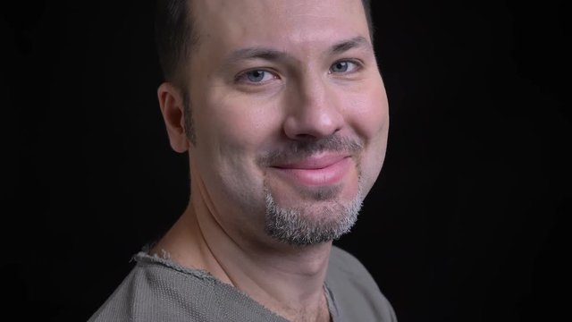 Portrait of middle-aged caucasian man with earring turns to camera and watches happily into camera on black background.