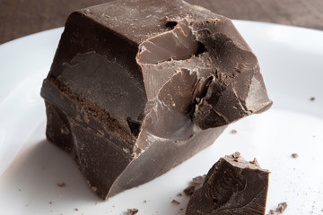 large chopped piece of chocolate on a white ceramic plate stands on a brown wooden table