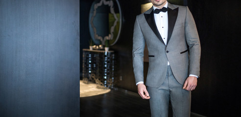 Man model in expensive custom tailored tuxedo, suit standing and posing inside luxury apartment