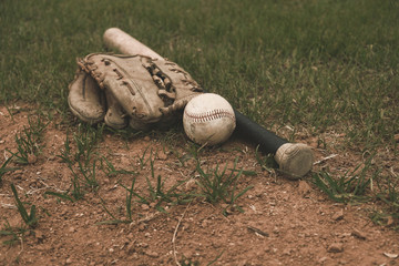 Old baseball with glove and bat lay on sports field.