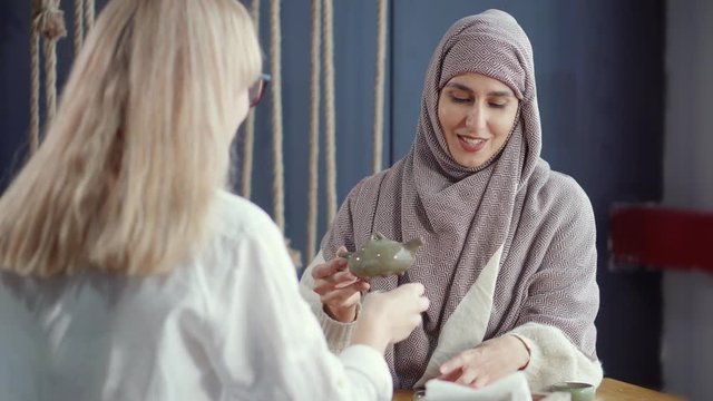 Women of muslim and western traditions are drinking tea together in cafe