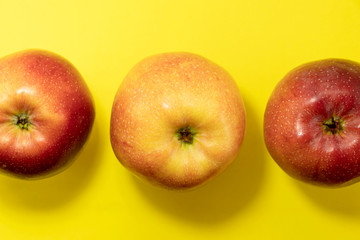 Three red ripe apples on a yellow background. View from above.