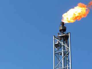 Gas flare is releasing and burning to the atmosphere at an offshore gas platform with sky.