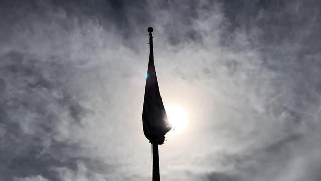 Tattered American flag flying in silhouette tangled on a flagpole trying to fly backlit by glaring sun