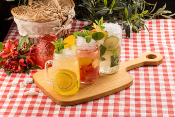Set cold lemonade with lemon, orange and peach on wooden board on textile napkin