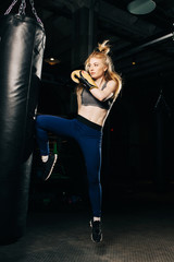 Obraz na płótnie Canvas Athlete woman in boxing gloves kicks black bag.