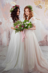Two charming brides in beautiful spring wreaths on their heads. Beautiful young women in wedding dresses