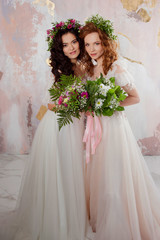 Two charming brides in beautiful spring wreaths on their heads. Beautiful young women in wedding dresses